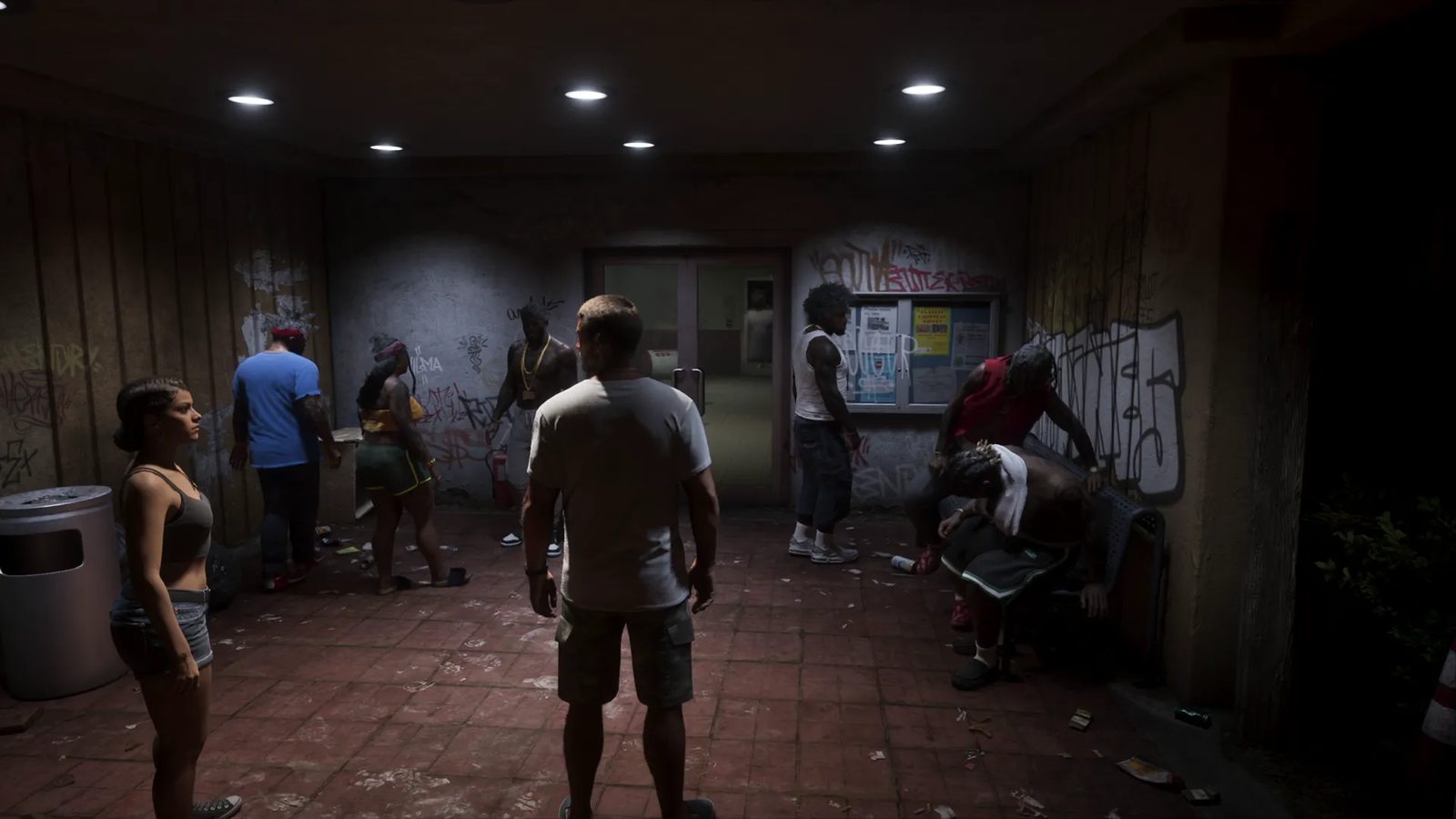A woman and a man in a white T-shirt stand in a dim, graffiti-covered tiled passage with a group of people near a noticeboard and double doors.
