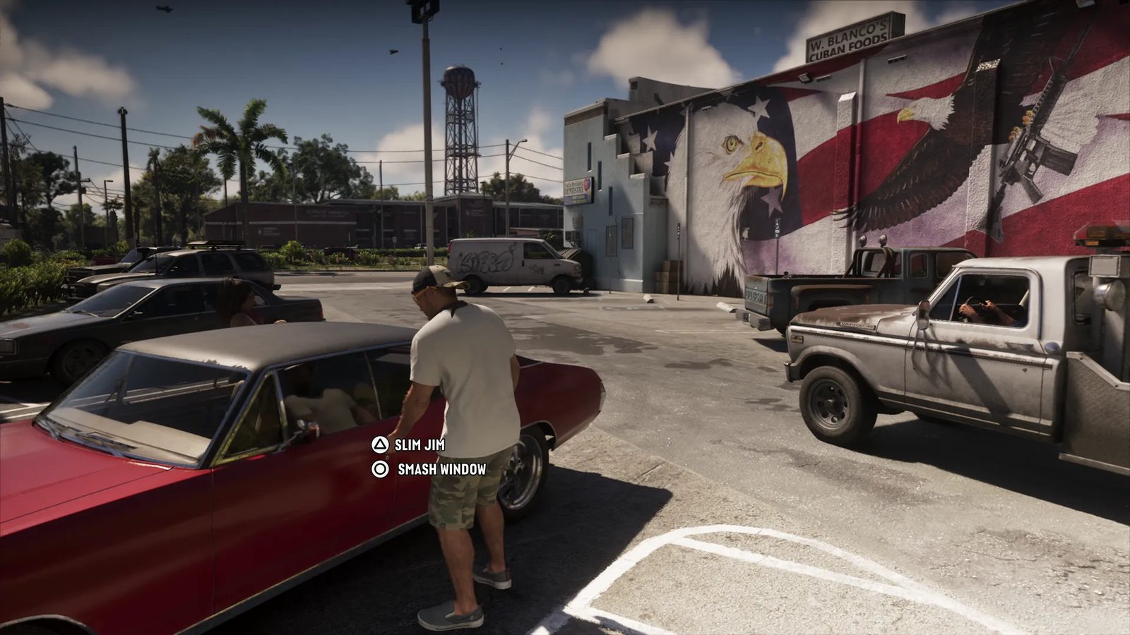 Jason Duval, in a cap, white T-shirt and camouflage shorts, stands by a red car in a sunny car park beside a building with an eagle and flag mural.