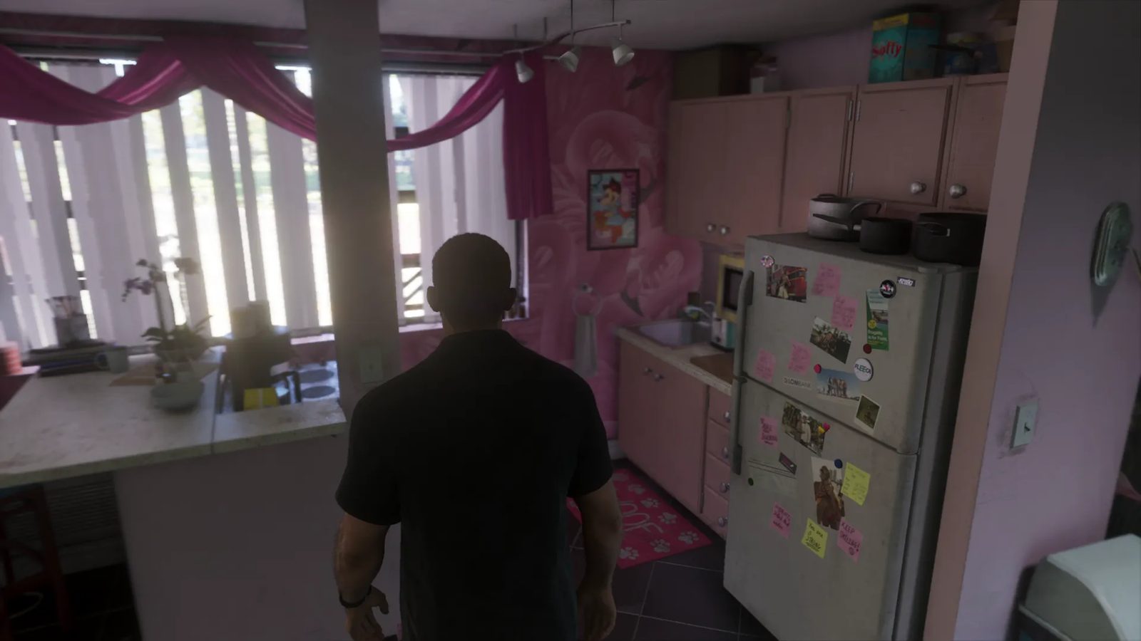 Jason Duval stands with his back to us in a small pink kitchen in Lucia's Apartment, beside a fridge covered in notes and photos.