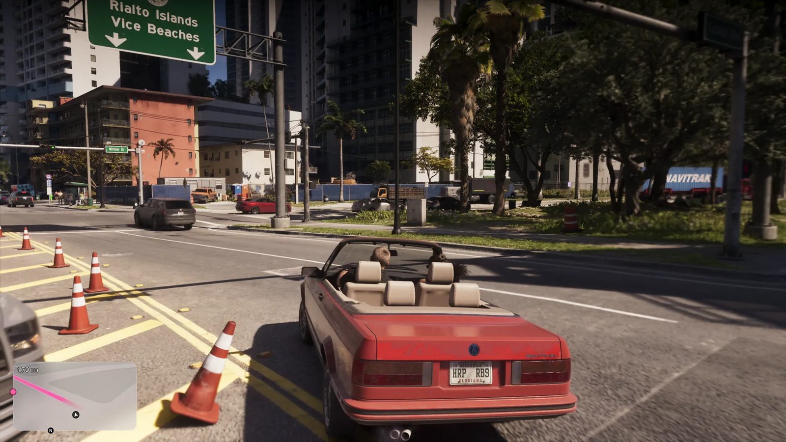 A red Übermacht Zion Cabrio with two people inside drives along a sunlit Vice City street past traffic cones and a green sign for Rialto Islands and Vice Beaches.
