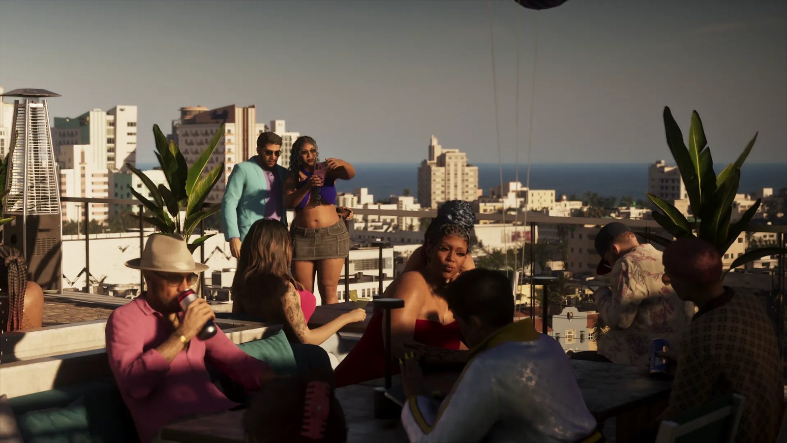 Groups of people drink and chat at tables on a sunlit rooftop terrace, with white seaside buildings and the sea behind them.