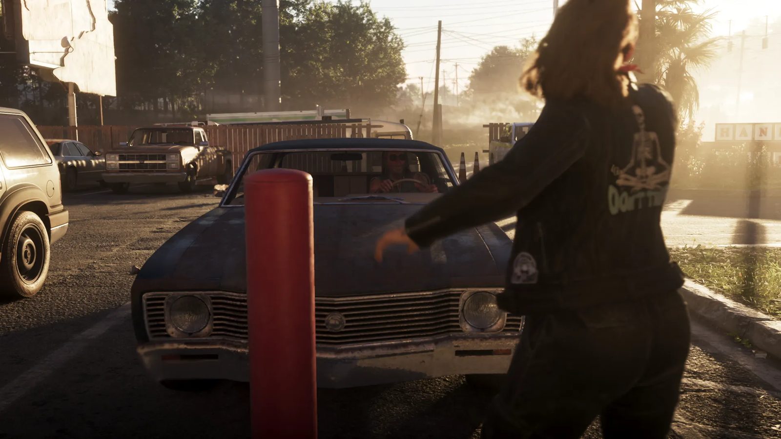 A woman in a black skeleton-print jacket walks past a red bollard towards a worn dark blue car with a driver in sunglasses, on a sunlit car park.