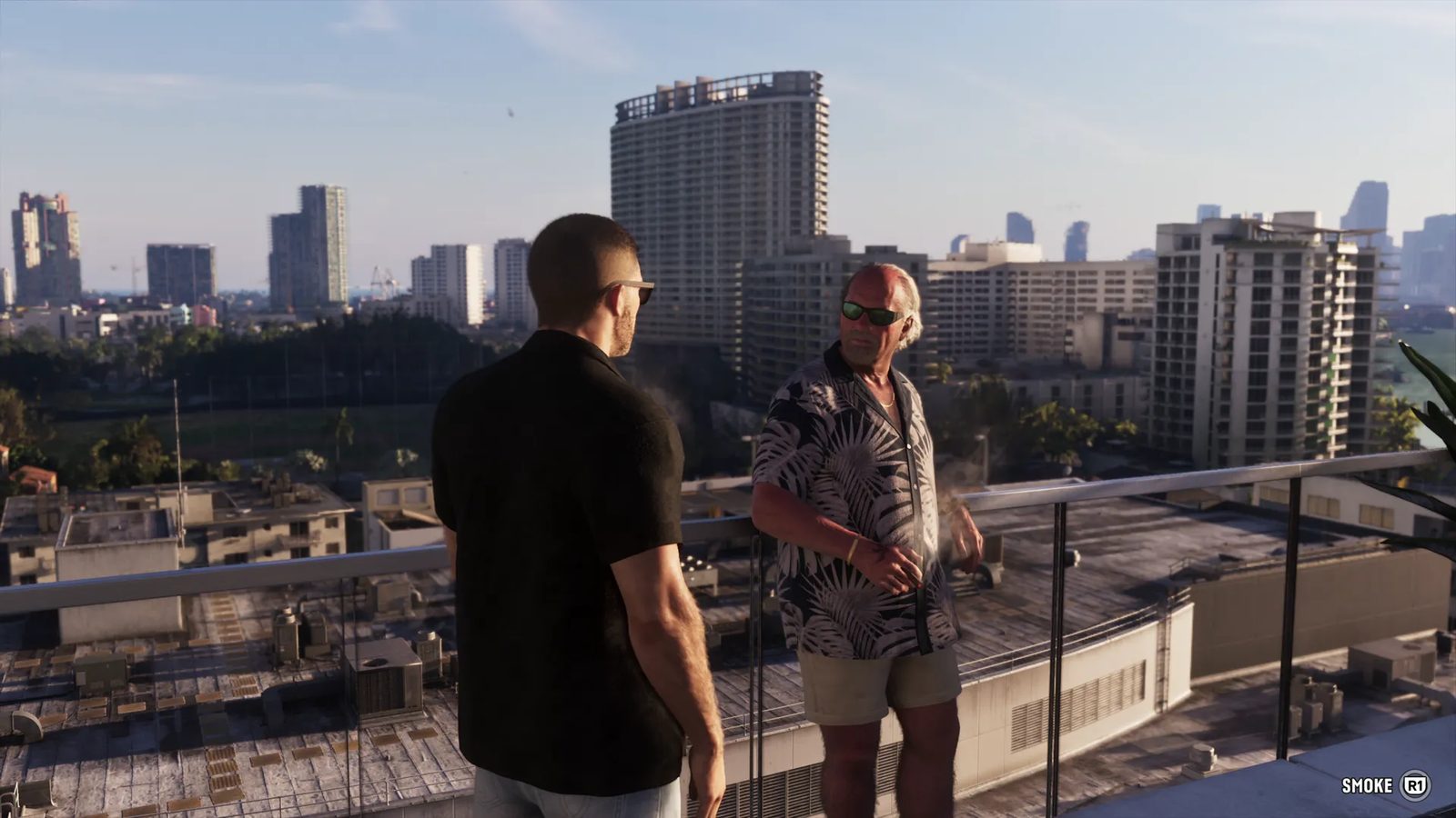 Two men in sunglasses talk on a rooftop terrace with a glass balustrade, high-rise blocks and low rooftops behind them in warm daylight.