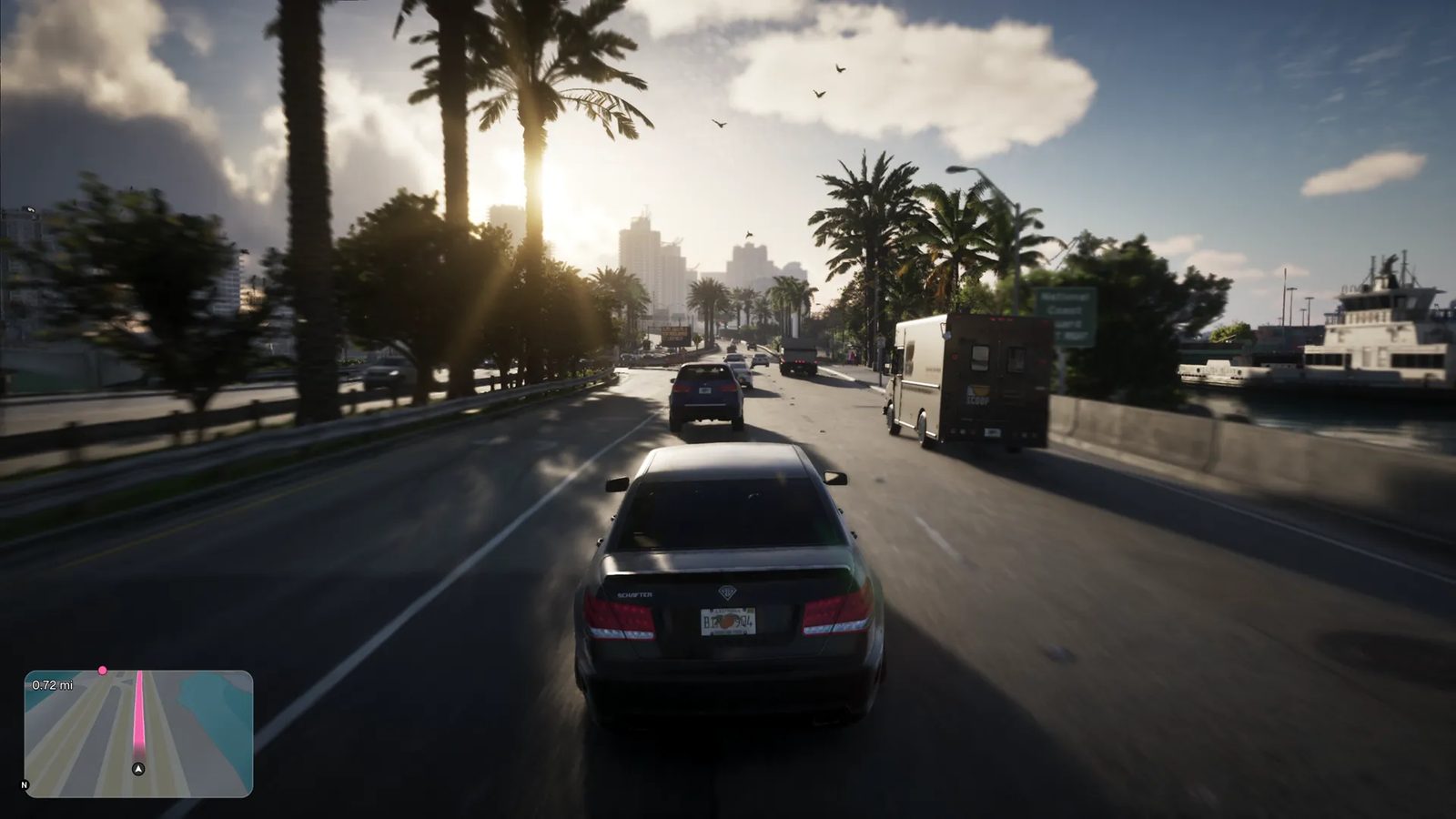 A dark grey saloon car drives along a sunlit, palm-lined coastal road in Vice City, following a Brute Boxville-style van, with city towers ahead.