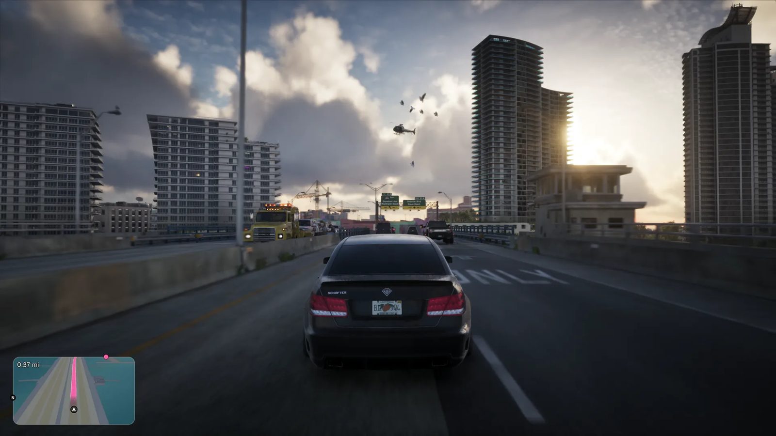 A dark Benefactor Schafter V12 drives along a raised road towards tower blocks at sunset, with a yellow Vapid Tow Truck and a helicopter ahead.