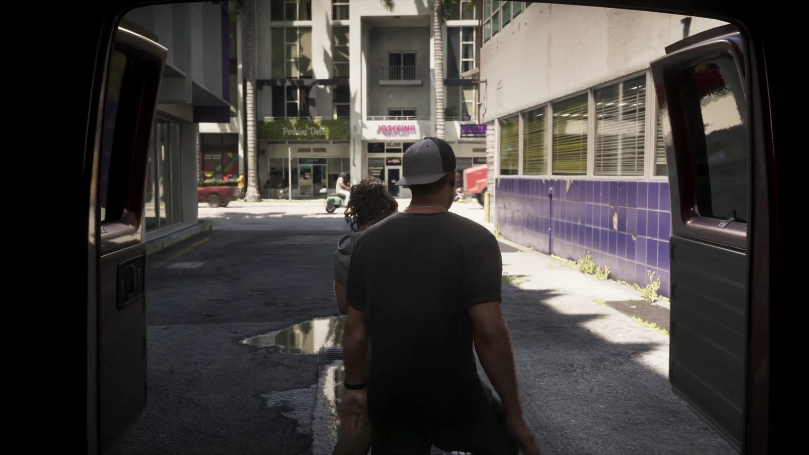 Jason Duval, in a grey cap and dark T-shirt, and Lucia Caminos walk away from the open back of a van along a sunlit city alley.
