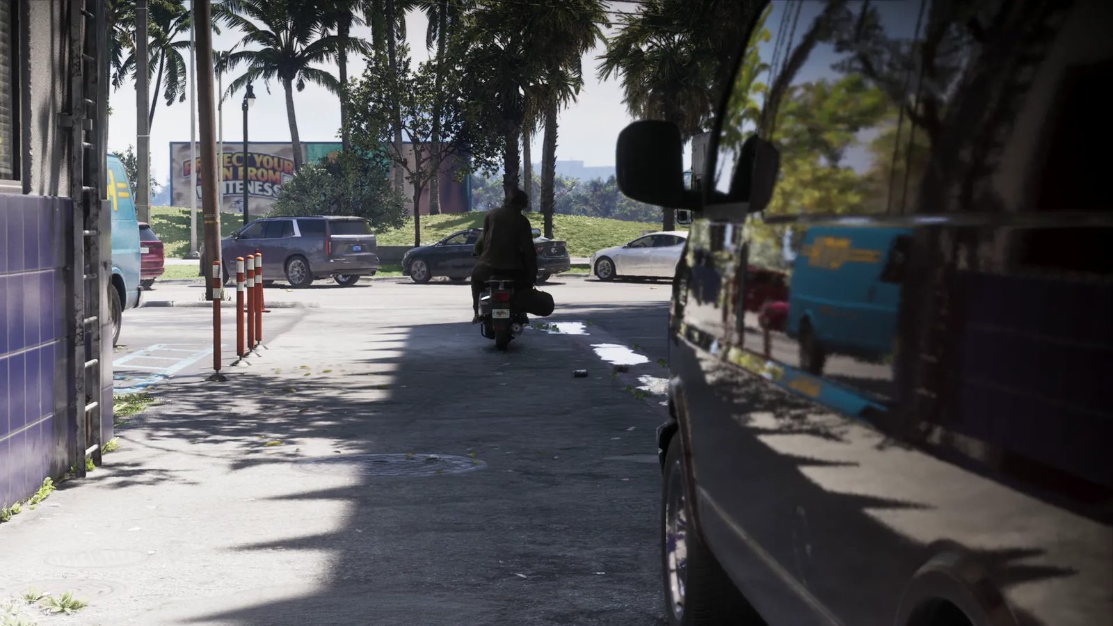 A rider on a motorbike, seen from behind, travels down a shaded back street lined with palm trees and parked cars, with a billboard in the distance.