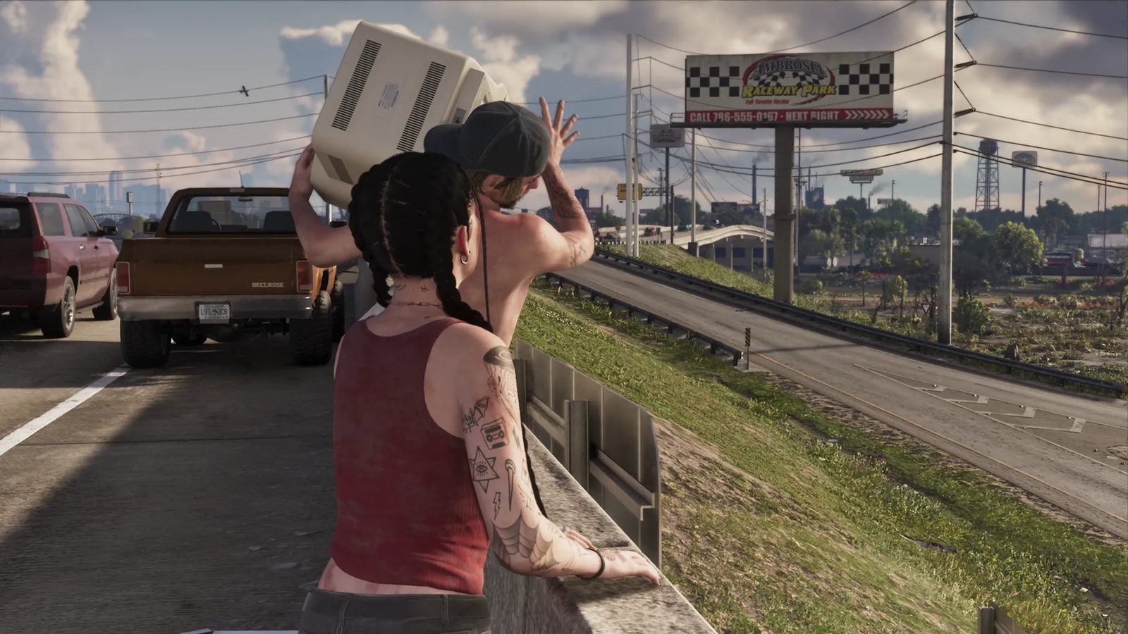 A woman with braids and arm tattoos leans on a roadside wall as a shirtless man in a cap carries a beige monitor, beside a Declasse pickup on a highway.