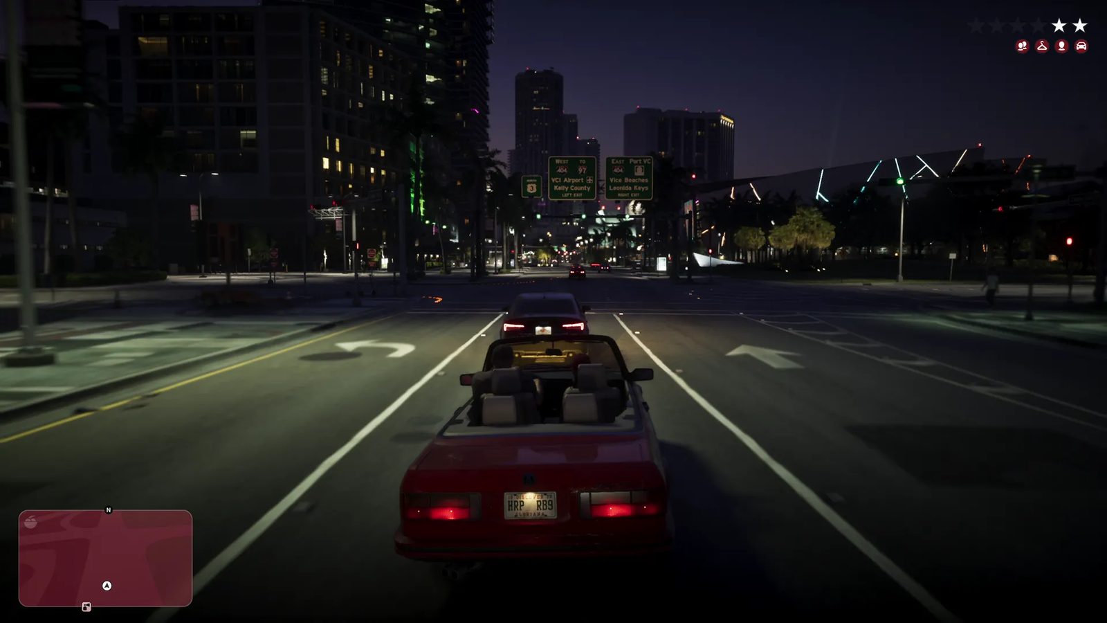 A red Ubermacht Sentinel Classic Cabrio drives along a wide city road at night in Vice City, following a dark saloon car under green road signs.