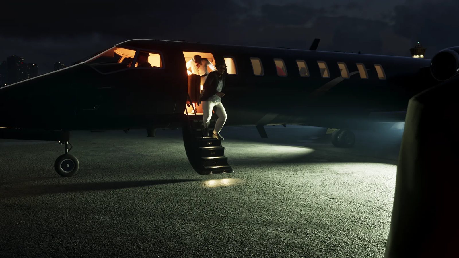 A man in a hat, dark jacket and white trousers steps down from a dark private jet at night, with another man in the lit doorway behind him.
