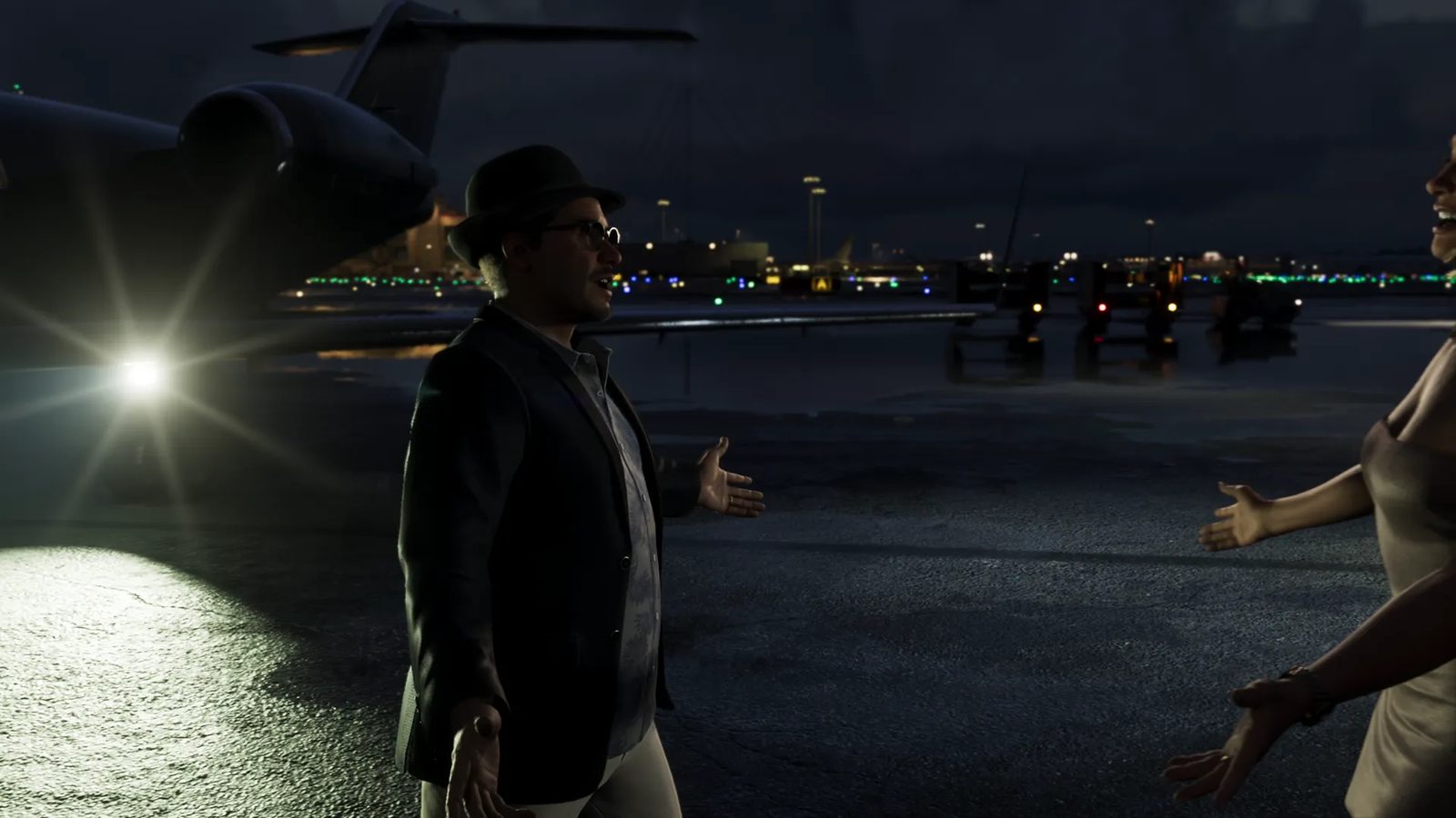 A man in a fedora, glasses and dark blazer holds his arms out to a laughing woman beside a private jet on an airport apron at night.
