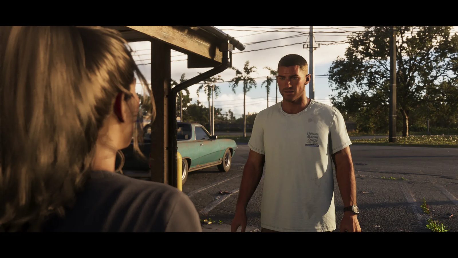 Jason Duval, in a pale Leonida Marine Center t-shirt, faces a woman seen from behind in a car park at sunset, with a rusty teal car behind.