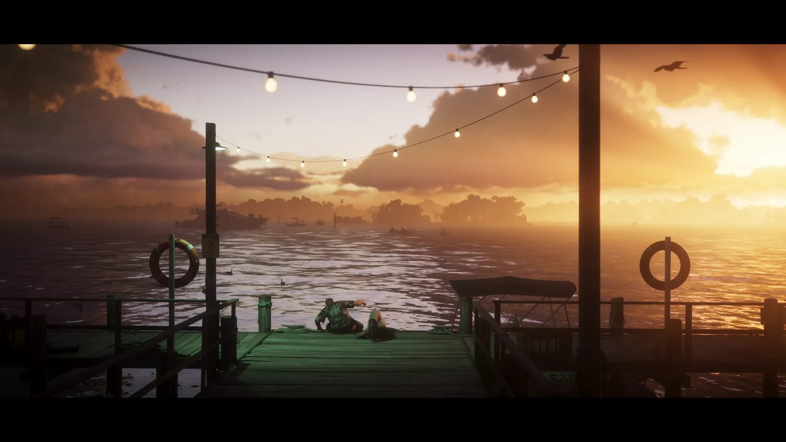 Two people lie and crouch on a wooden jetty at sunset, with string lights overhead and boats on the water beyond, in the Leonida Keys.