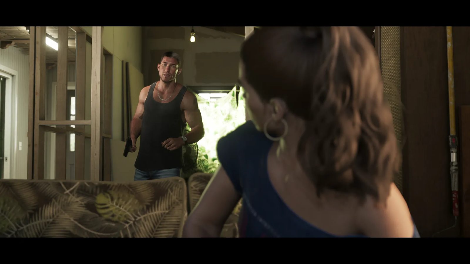 Jason Duval stands in a half-finished room holding a handgun while a woman, seen from behind, looks back at him.