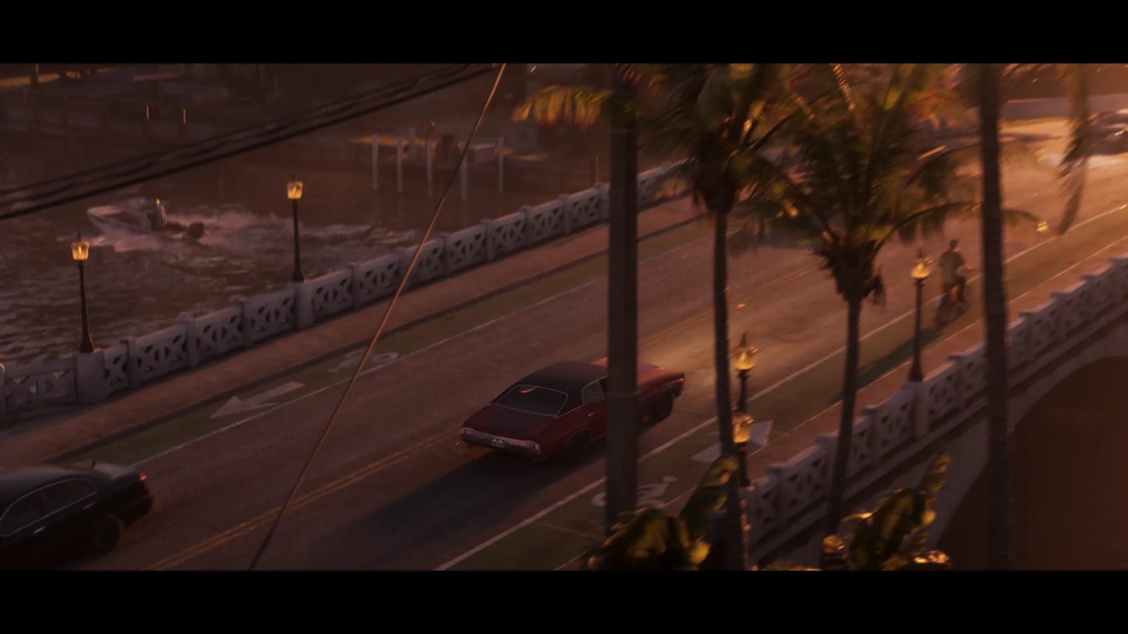 A dark red classic muscle car drives along a palm-lined bridge over a canal at sunset, with a speedboat on the water and a cyclist nearby.