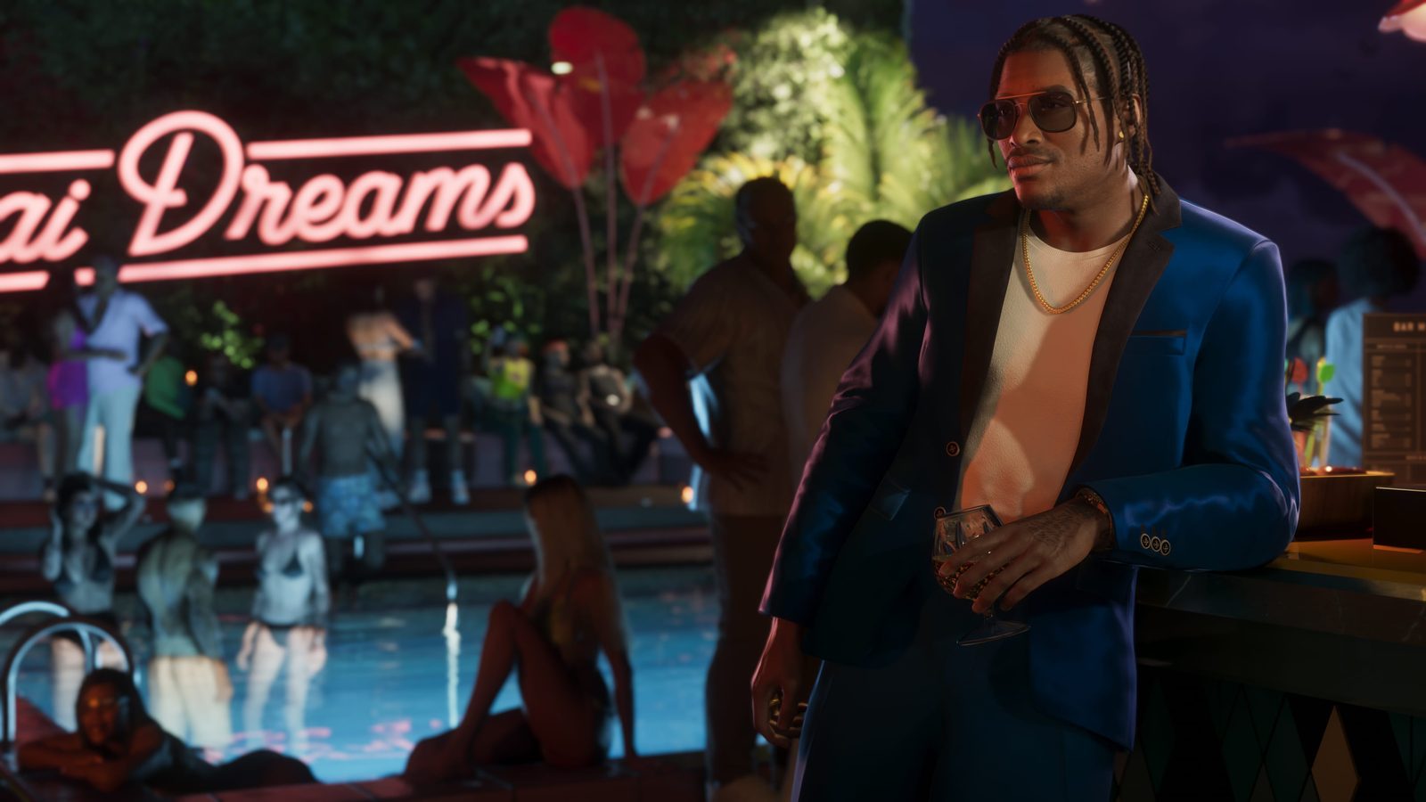 Dre'Quan Priest, in a blue suit and sunglasses, leans on a bar holding a glass, with a lit pool and a neon sign behind him at night.