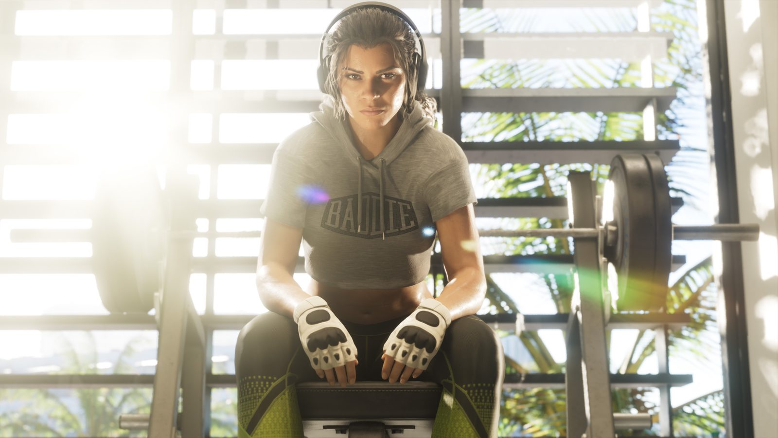 Lucia Caminos sits on a weight bench in a sunlit gym, wearing headphones and fingerless gloves, with a loaded barbell beside her.