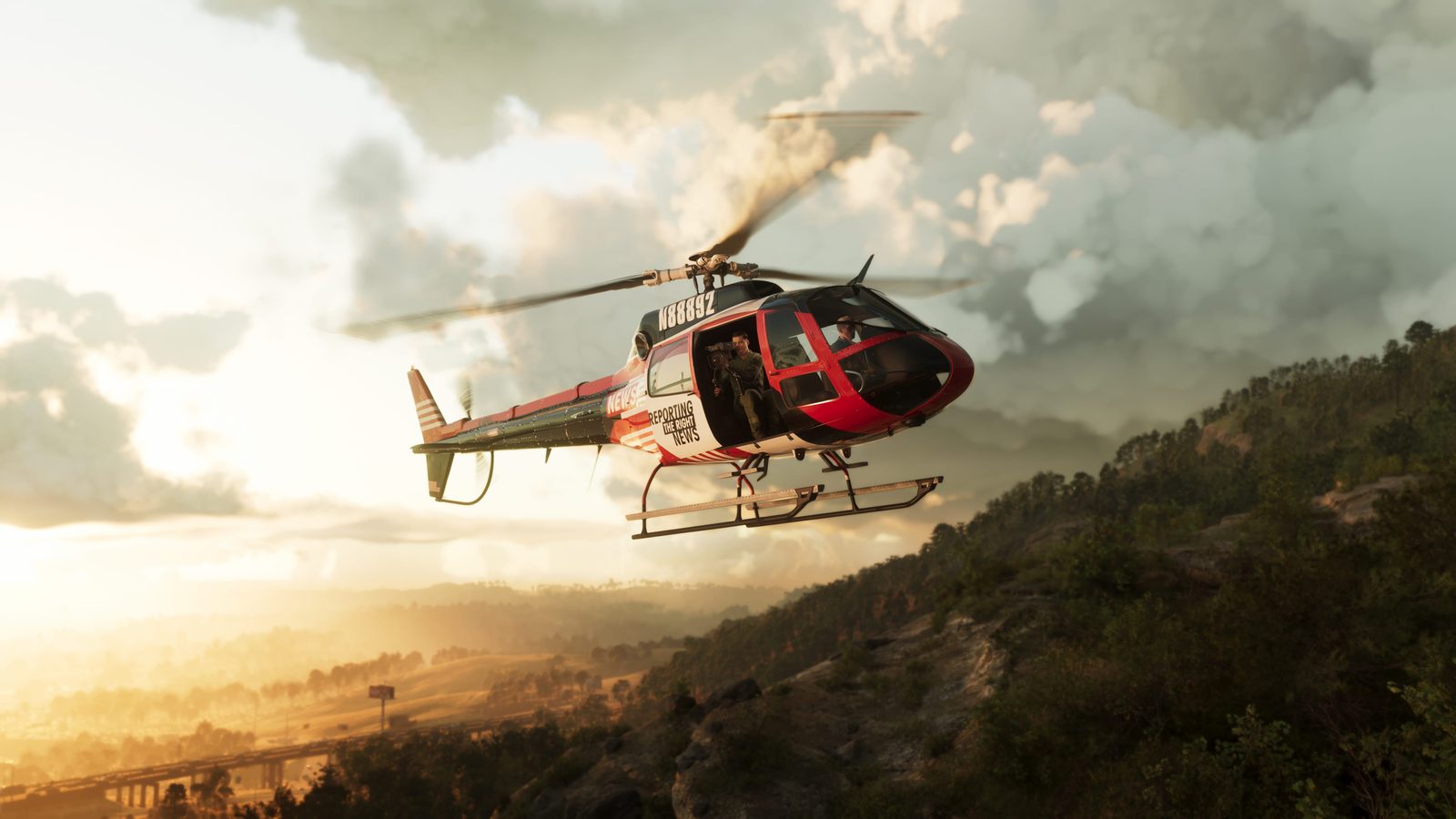 A red and white Buckingham News Maverick helicopter hovers beside a wooded hillside at sunset, with a cameraman in the open side door.