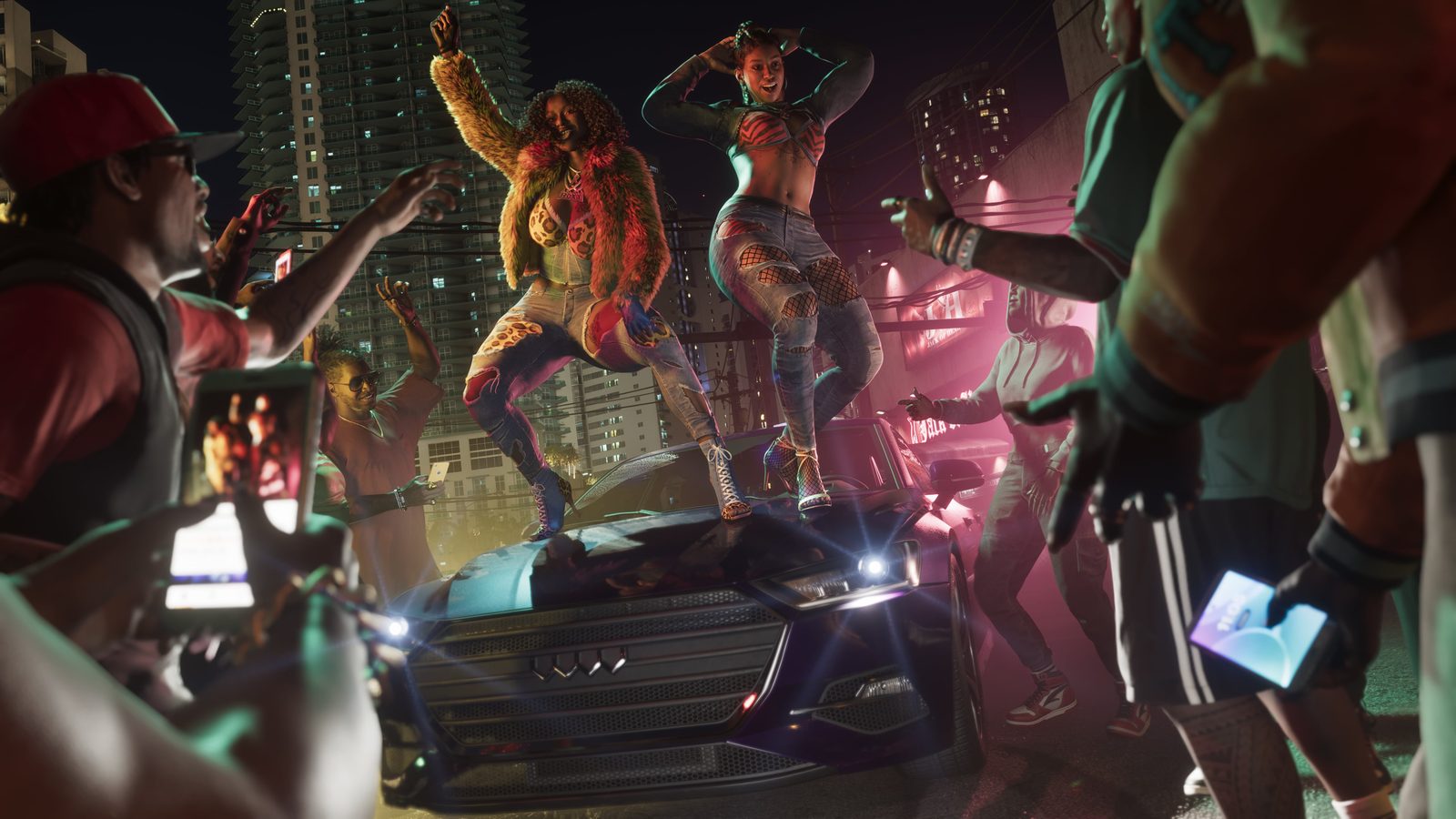 Two women dance on the bonnet of a dark sedan at night while a crowd films them on phones, with high-rise towers behind.