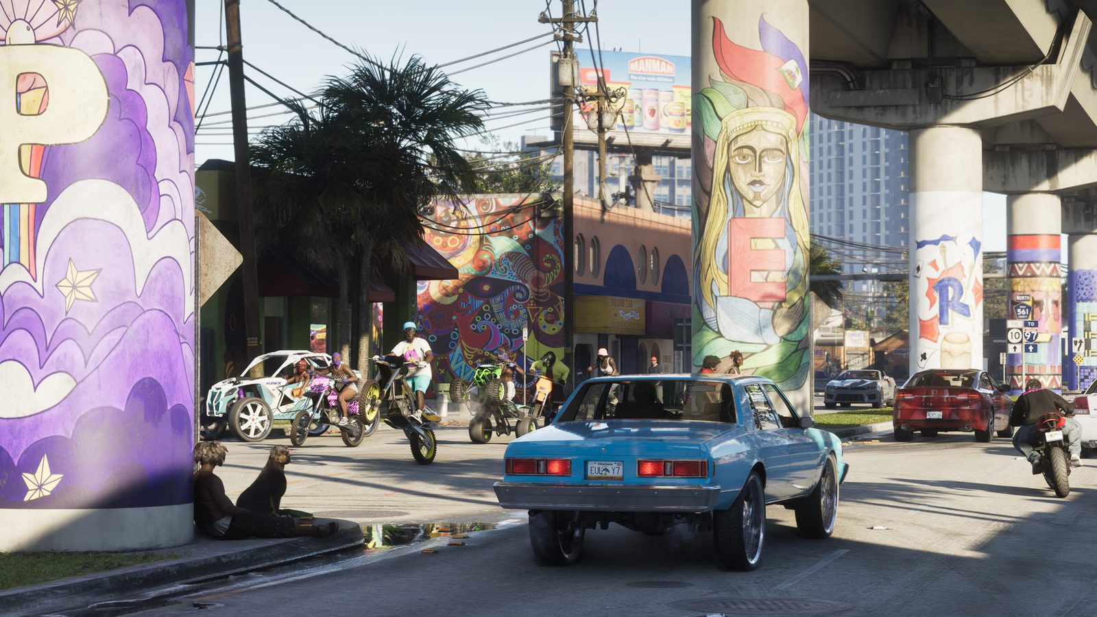 A light blue lowered car with chrome wheels drives under a flyover past riders on dirt bikes and quads, with painted murals on the pillars.