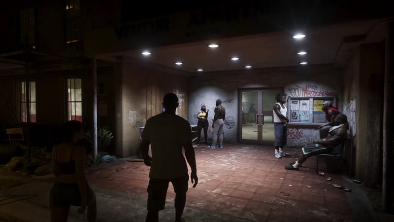 A man and a woman in silhouette face a group of people outside a graffiti-covered apartment entrance under bright ceiling lights at night.