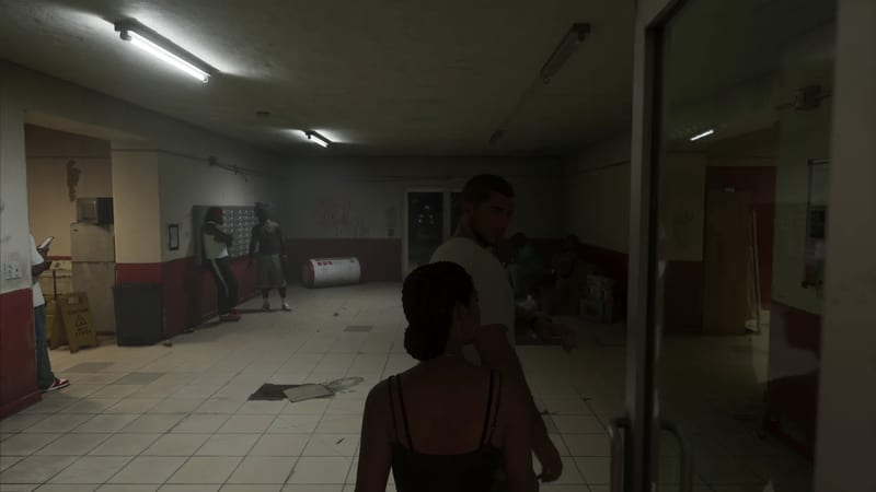 A woman with braided hair and a man in a white t-shirt walk through a dim, run-down apartment lobby where other people stand near the mailboxes.