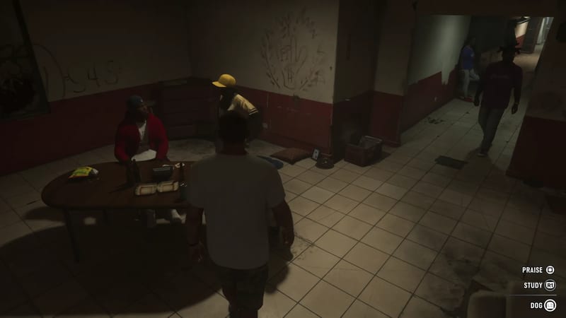 A man in a white T-shirt faces a seated man in a red jacket at a table in a dim tiled room, with two other men nearby.