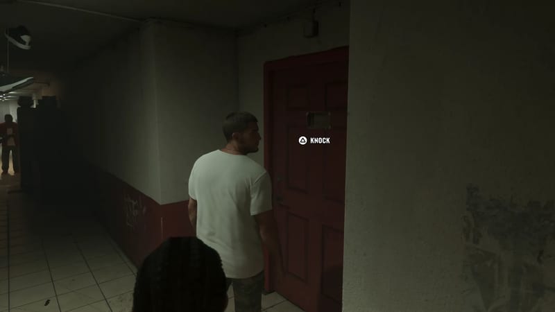 A man in a white T-shirt stands facing a red door in a dim, tiled corridor, with a "Knock" prompt beside it.