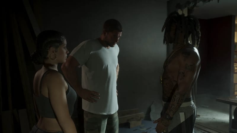 Lucia Caminos and Jason Duval stand in a dim, rundown room facing a tattooed, shirtless man with long dreadlocks.