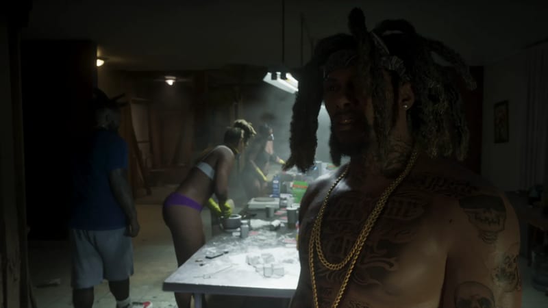 A shirtless, tattooed man with dreadlocks and gold chains stands in a dim, smoky room where people work at a table covered in white powder.