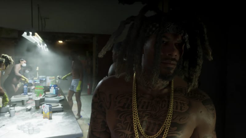 A shirtless man with dreadlocks, a bandana and gold chains stands in a dim warehouse where masked workers pack white powder at a long table.