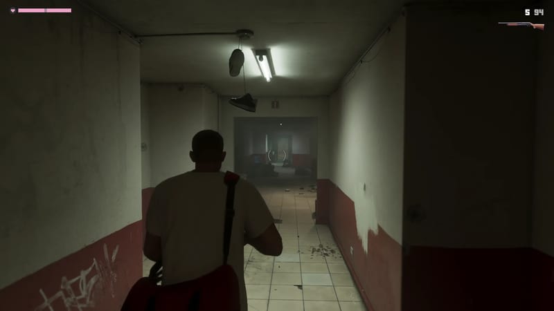 A man in a cream t-shirt with a red shoulder bag walks down a dim, tiled corridor with red-and-cream walls, holding a shotgun.