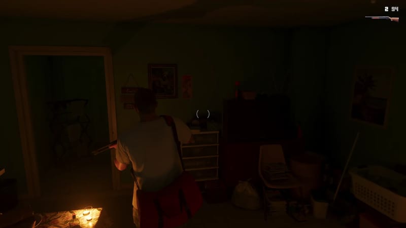 A man in a white t-shirt with a red shoulder bag holds a shotgun in a dimly lit, cluttered room lit by candles, seen from behind.