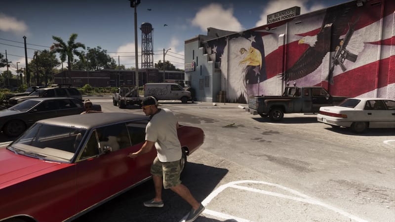 A man in a cap, white T-shirt and camouflage shorts opens the door of a red car in a car park beside a large eagle and flag mural.
