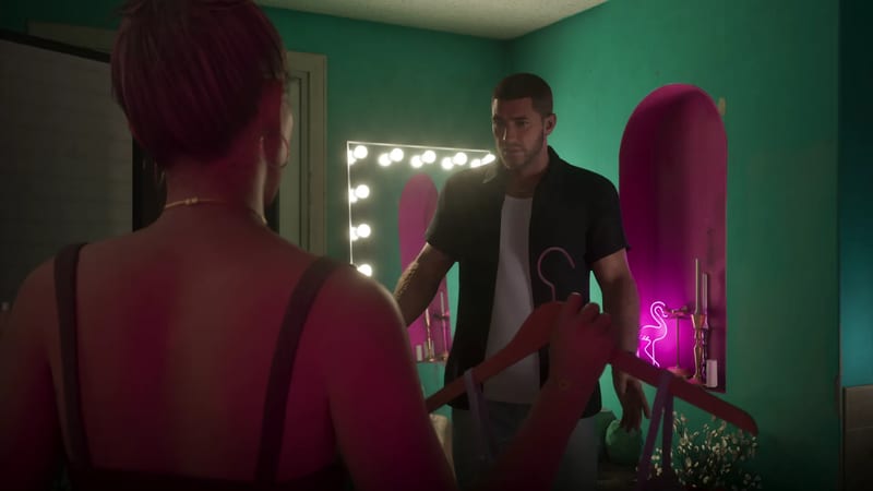 Seen from behind, a woman holds a red coat hanger and faces Jason Duval, who stands in a green room with a lit mirror and a pink neon flamingo.