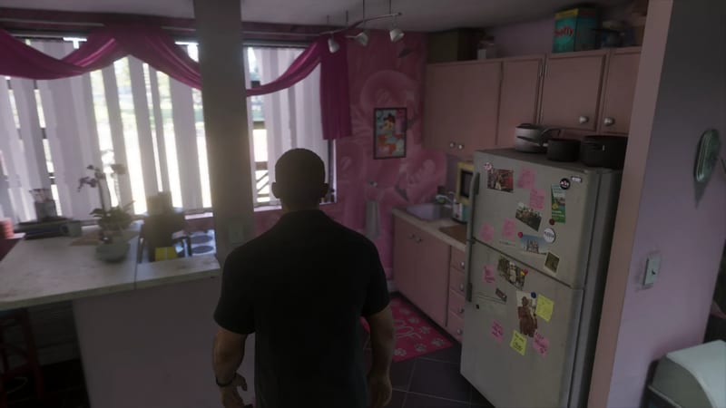 Jason Duval stands with his back to us in a small pink kitchen in Lucia's Apartment, beside a fridge covered in notes and photos.