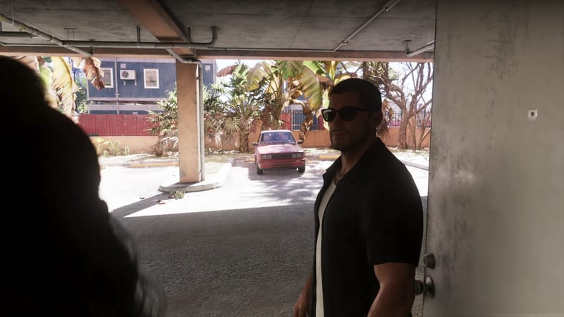 Jason Duval, in sunglasses and a black shirt, stands in a covered car park beside an open door, with a red car parked outside in the sun.