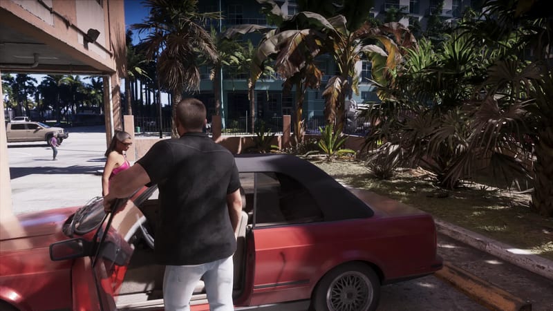 Jason Duval stands at the open door of a red convertible with a black roof, as a woman in a pink top walks past under tall palms and a tower block.