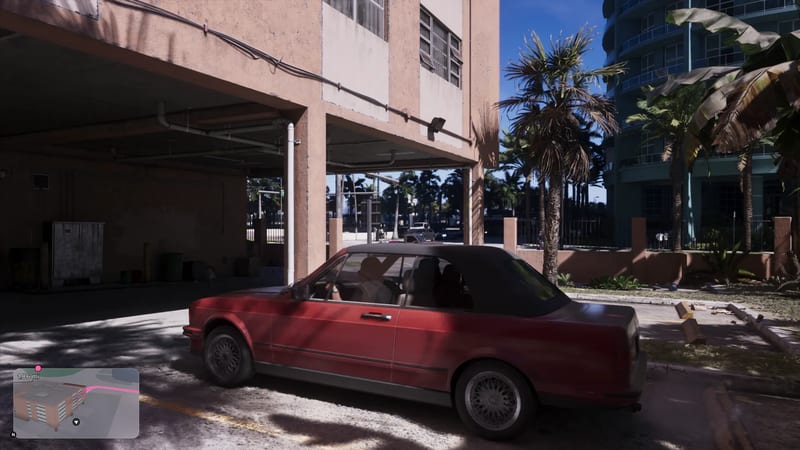 A red convertible with a black soft top is parked beside a pink concrete building, with palm trees and a curved blue tower behind it on a sunny day.