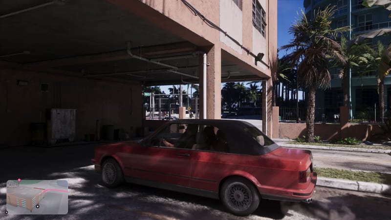 A dusty red convertible with a black roof drives out from under a pink concrete building towards a sunlit street lined with palm trees.