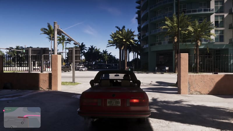A red convertible with a Louisiana plate drives towards a sunlit junction in Vice City, with palm trees and a tall teal apartment block beside the road.