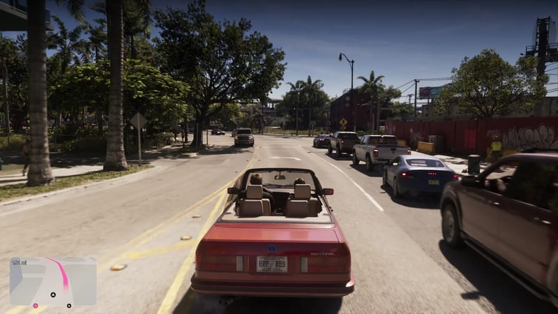 A red convertible with two people in it drives along a sunny Vice City road lined with palm trees, with queued pickups and cars on the right.