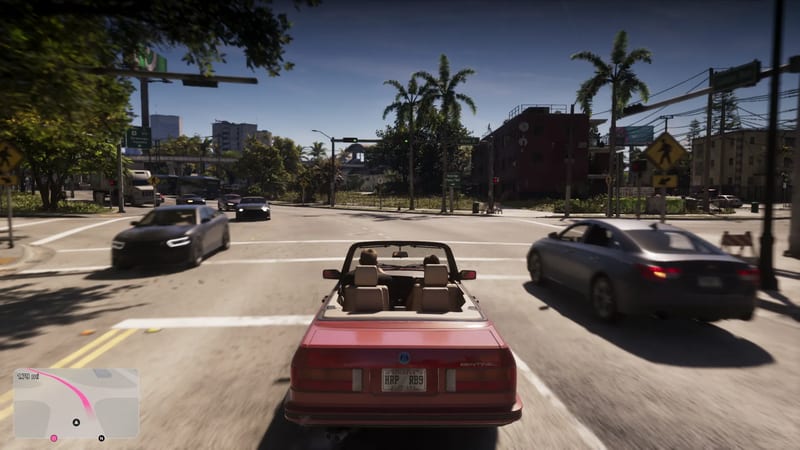 A red convertible with two people in it drives through a sunny Vice City junction lined with palm trees, with other cars passing either side.