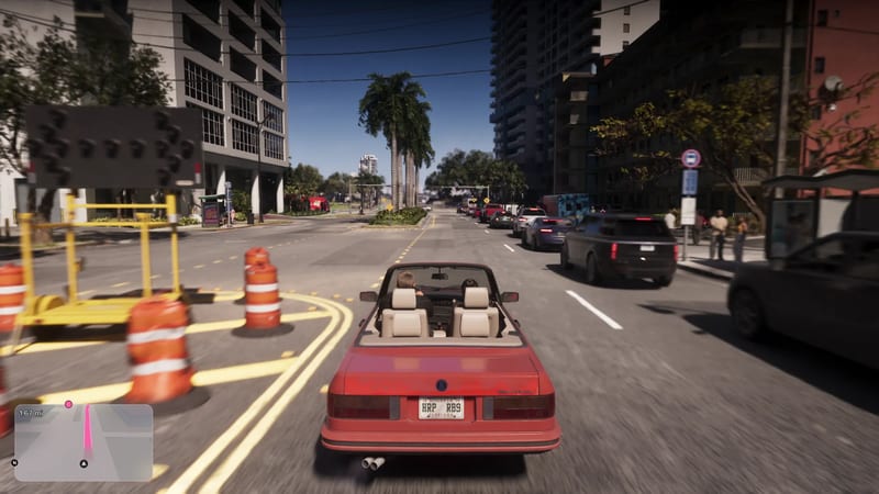 Two people in a red convertible with cream seats drive along a palm-lined Vice City street past orange traffic barrels and queuing cars.