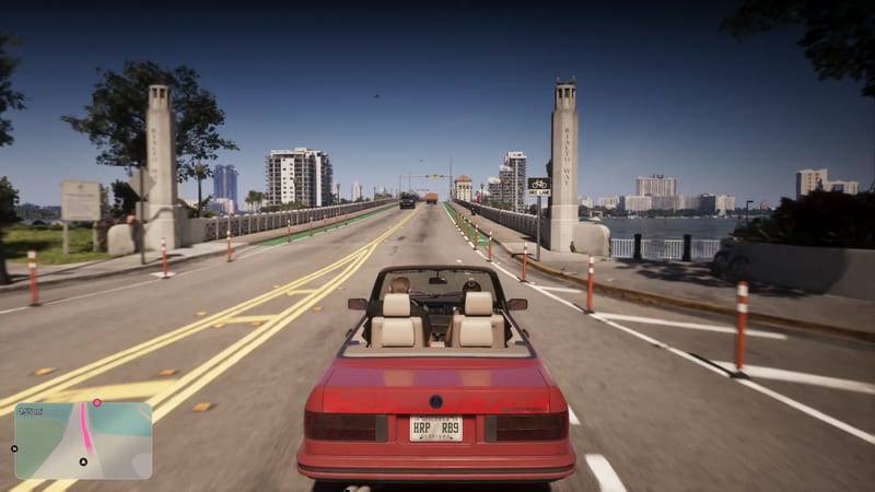 A red convertible with two people in cream seats drives along a bridge in Vice City, between stone pillars marked Rialto Way, on a clear day.