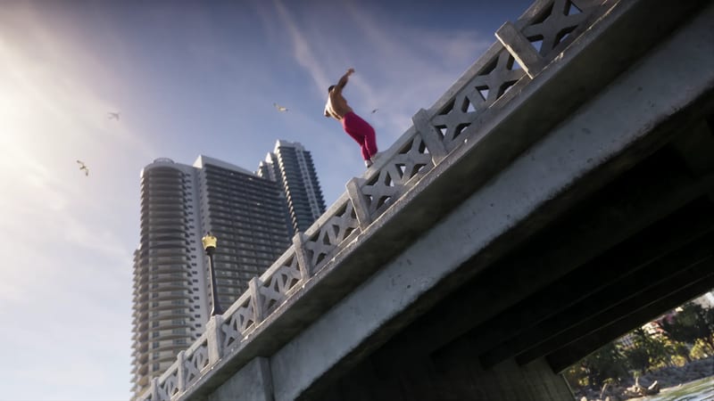 A shirtless man in bright pink trousers leaps from the stone railing of a bridge, with tall apartment towers and gulls behind him against a sunlit sky.