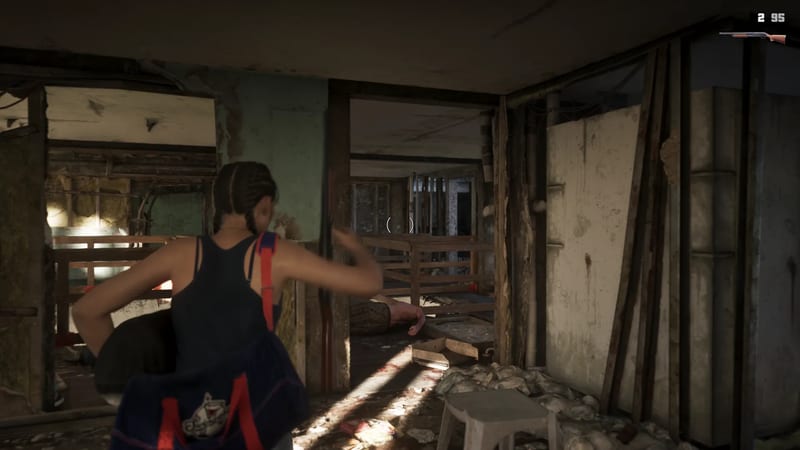 A woman with braided hair and a navy holdall walks through a derelict, dimly lit building with exposed beams, past a figure lying on the floor.
