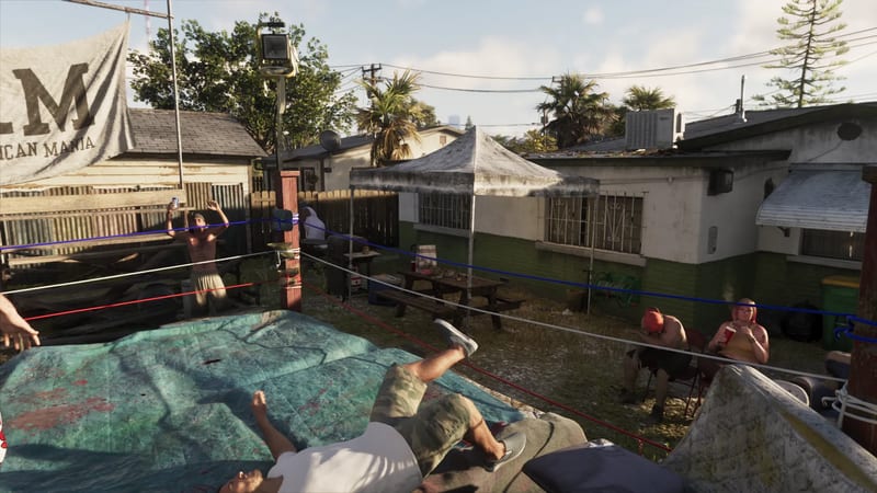 A man in a white T-shirt and camouflage shorts falls backwards onto a tarpaulin-covered backyard wrestling ring as onlookers watch in the afternoon sun.