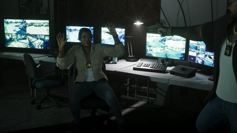 A woman in a beige shirt sits at a security desk with her hands raised while a man off-screen points a handgun at her.