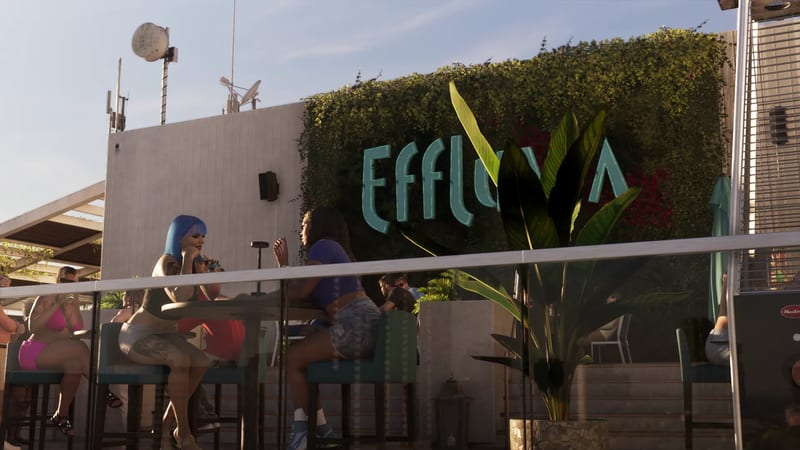 Two women sit at a table on a sunny rooftop terrace, in front of a green hedge wall with a large teal Effluvia sign.